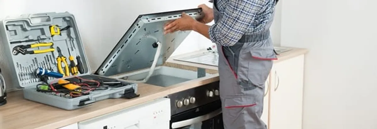 Cooktop repair technician lifting a built-in stovetop for service in Arlington, TX